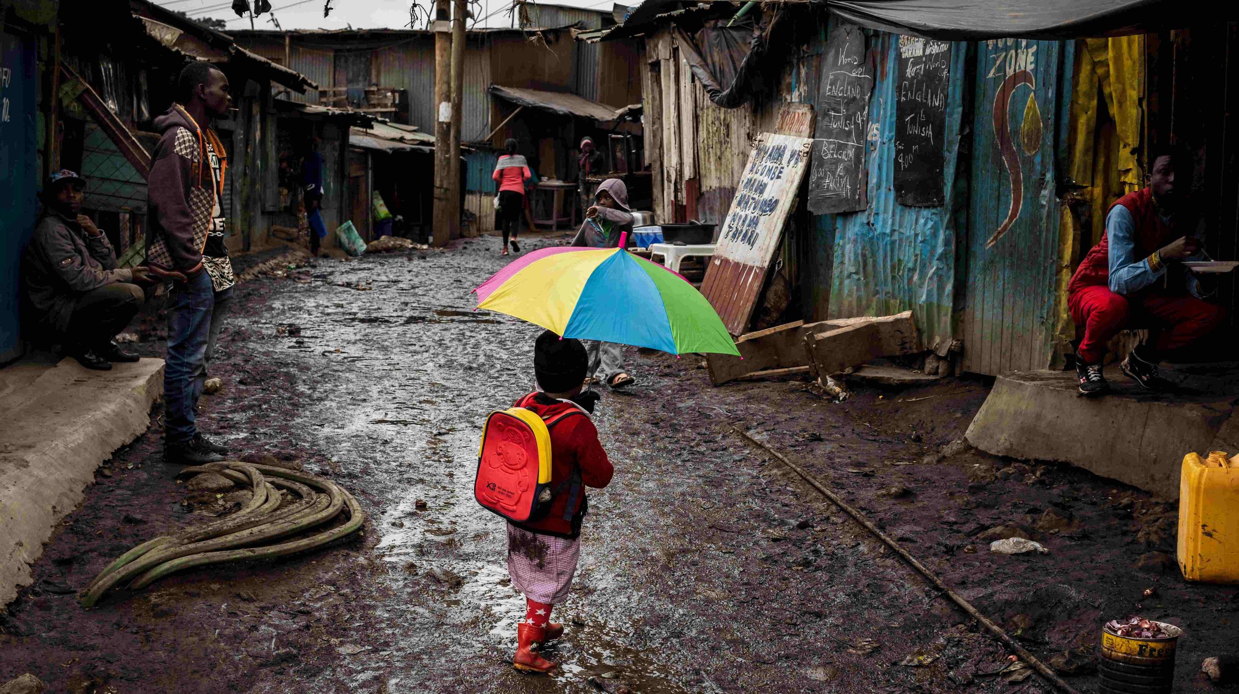 Ein Mädchen läuft mit einem bunten Regenschirm durch eine schlammige Straße in einem Slum in Nairobi. (Quelle: Lars Heidrich)